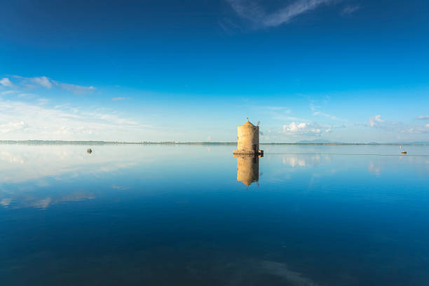 Historic spanish windmill perfectly mirrored in tranquil blue lagoon waters in Monte Argentario, province of Grosseto, Tuscany region, Italy.