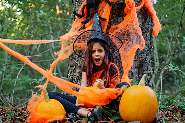 istock Child in witch costume surrounded by pumpkins and Halloween decorations in a forest setting during autumn 2235859258