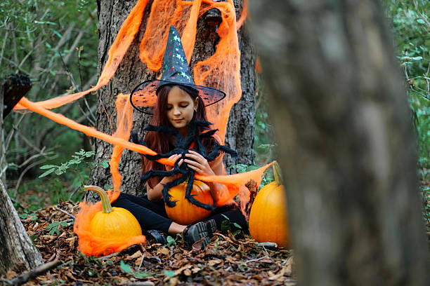 istock Child dressed as a witch sitting among pumpkins in a forest during Halloween festivities 2235859263