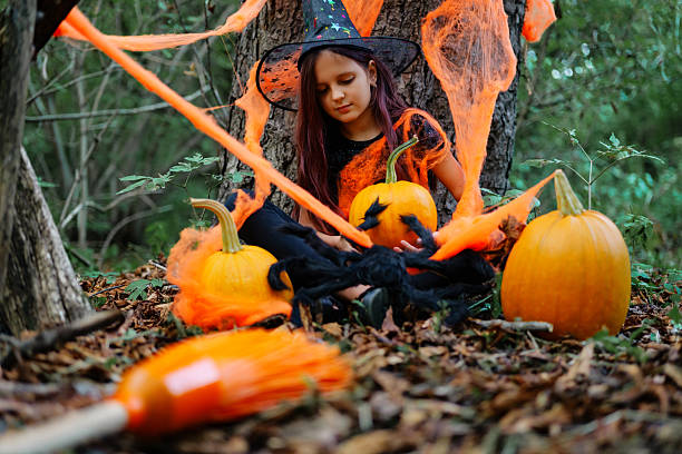 istock Child in witch costume surrounded by pumpkins and decorations on a forest floor during Halloween festivities 2235859270