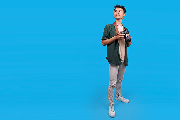 Young Man With A Camera Looking Aside to Copy Space On A Blue Background