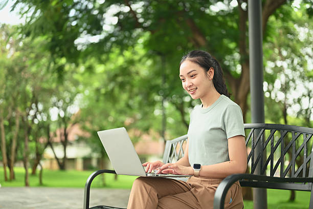 istock Young woman sitting on a park bench using a laptop, enjoying remote work in a natural 2235865344