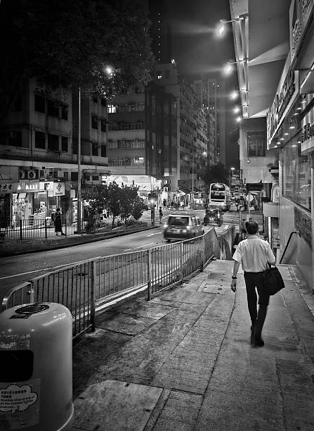 Rear View of a man walking on a sidewalk in Hongkong at night. Black and white.