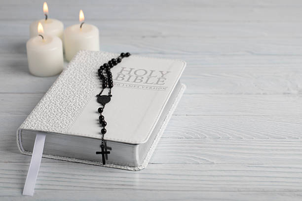 Holy bible and rosary with candles on white wood background