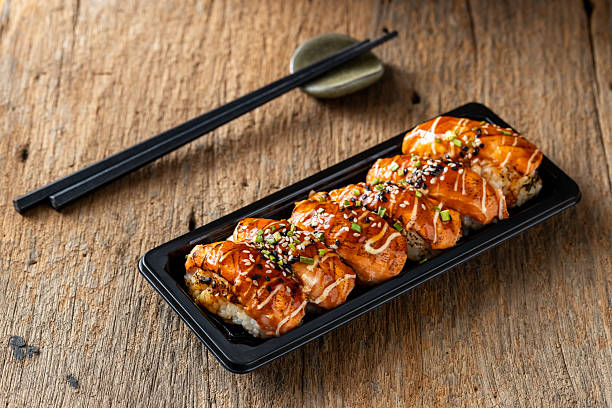 istock Delicious salmon sushi rolls served on black plate with chopsticks 2235871870