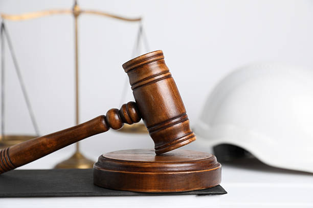 istock Accident at work concept. Gavel, scales and construction worker's protective gear on white wooden table, selective focus 2235872313