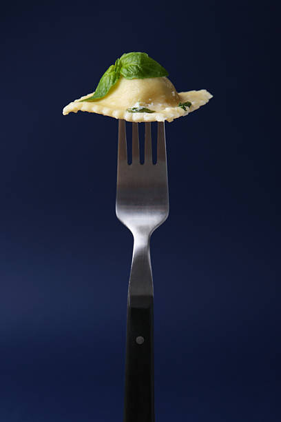 Delicious ravioli with cheese and basil on fork against dark blue background, closeup