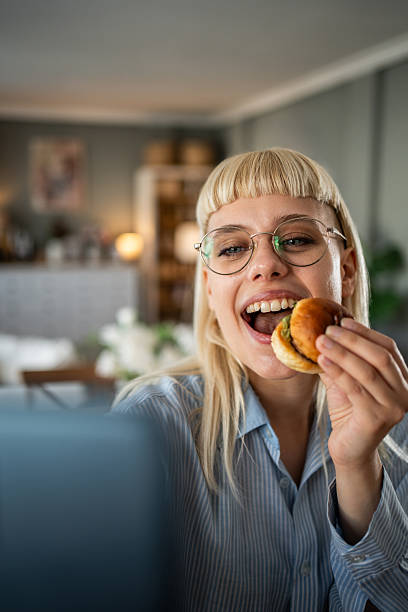 istock Happy young woman eating sandwich while working on laptop 2235873140