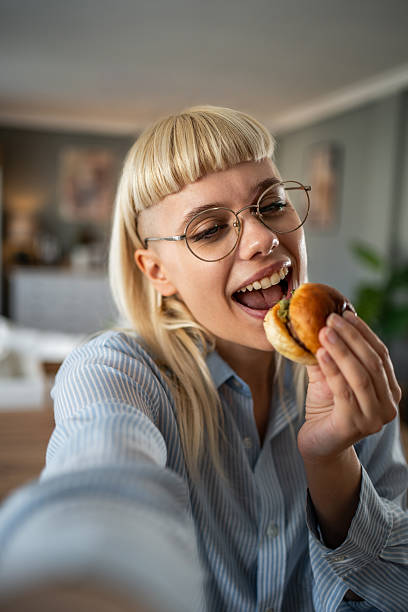 istock Young woman taking a selfie while enjoying a burger at home 2235873155