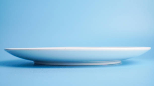 eye level view of empty ceramic white plate on light blue background