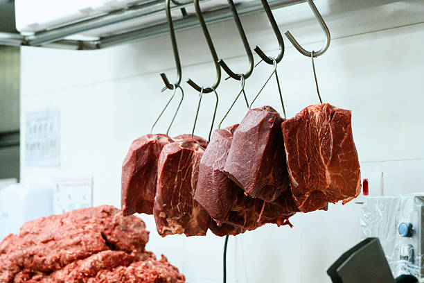 Portrait of a friendly butcher at his place of work facing the camera smiling wearing a white uniform and a red apron - People at work concepts