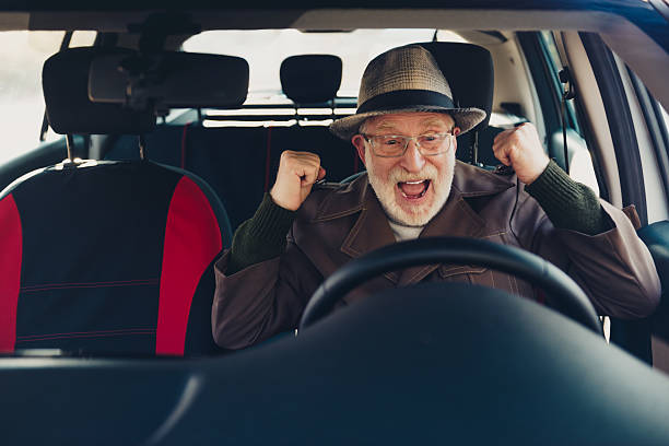 istock Happy elderly man cheering with excitement while sitting in a car on a sunny day, enjoying the new driving experience 2235880704