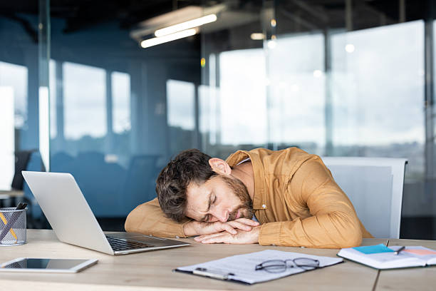 istock Tired man sleeping on laptop at desk in modern office environment 2235882716