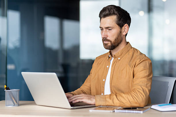istock A businessman diligently works on his laptop in a modern office setting, showcasing concentration and productivity. 2235882755