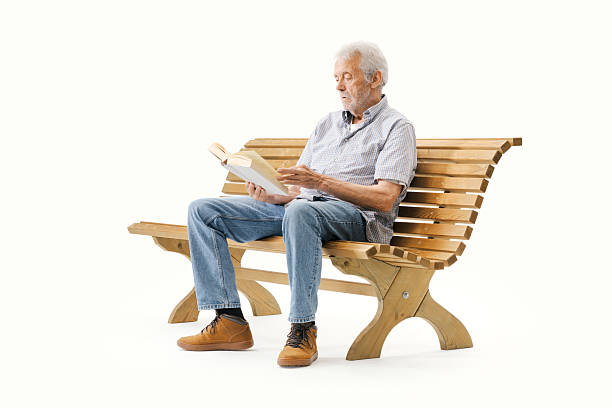 Relaxed senior man sitting on a wooden bench and reading a book, isolated on white background