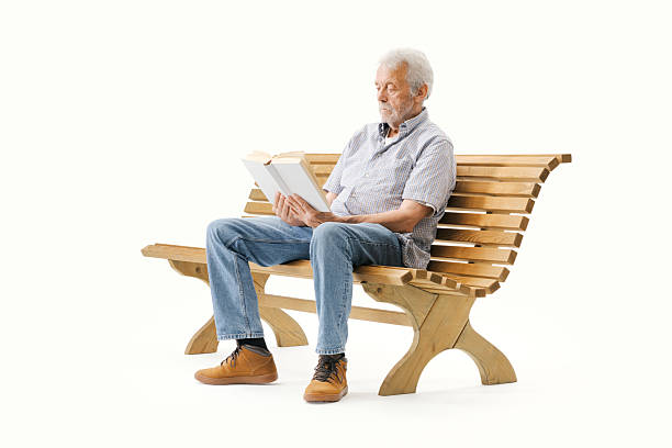 Relaxed senior man sitting on a wooden bench and reading a book, isolated on white background