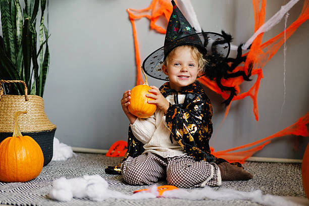 istock Child dressed as a witch sits happily with a pumpkin amidst colorful Halloween decorations in a cozy indoor space 2235883877