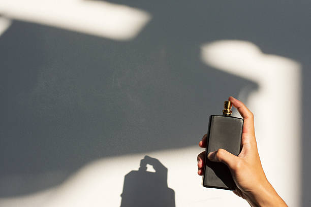 Male hand spraying perfume bottle with natural light and shadow on a white background