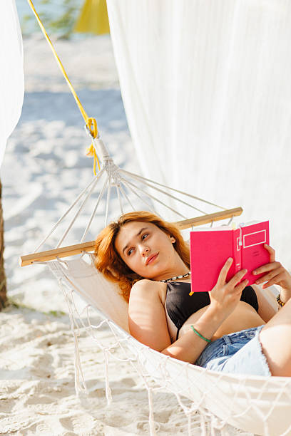 istock Woman Relaxing on Hammock with Book on Sandy Beach During Summer Vacation 2235885637