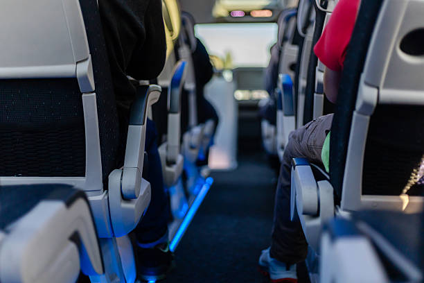 Passengers sit in a bus with their backs visible, bright lighting highlighting the aisle as sunlight filters through the windows on a pleasant afternoon journey.