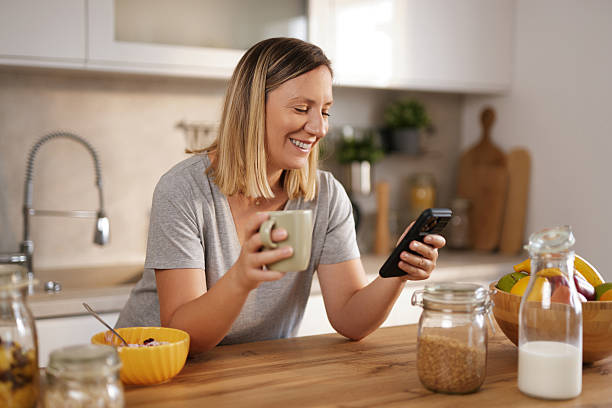 istock Smiling woman enjoying breakfast and checking her phone in the kitchen 2235887348