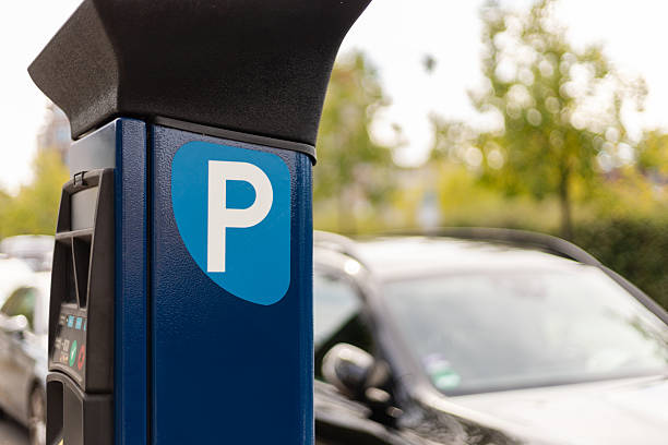 istock A parking meter is prominently displayed in a clean parking lot surrounded by greenery. Several cars are parked nearby, suggesting a bustling area during the day 2235887949