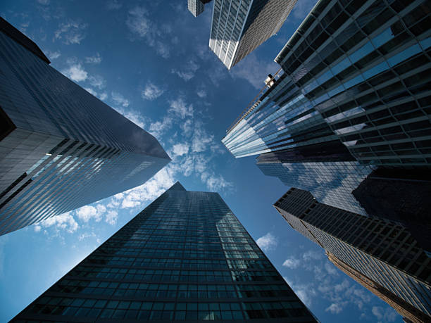 istock Looking Up at New York City Skyscrapers - A dramatic low-angle view of multiple modern skyscrapers reaching into a deep blue sky with white clouds, showcasing the urban canyon effect. 2235888772