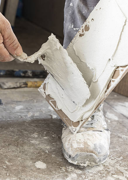 istock Craftsman spreads tile adhesive with notched trowel on a tile back, closeup. Construction process 2235890535