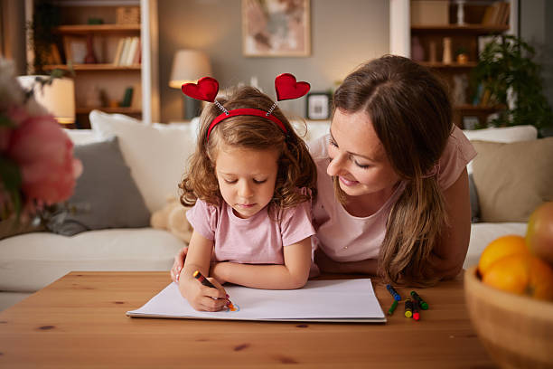 Mother watching her daughter drawing with crayons in the living room