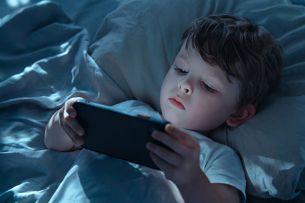 istock Child Using Smartphone in Bed Showing Gadget Addiction 2235891155