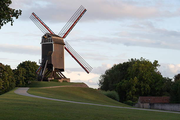A picturesque windmill stands majestically on a hill, embraced by vibrant greenery and a serene sky.