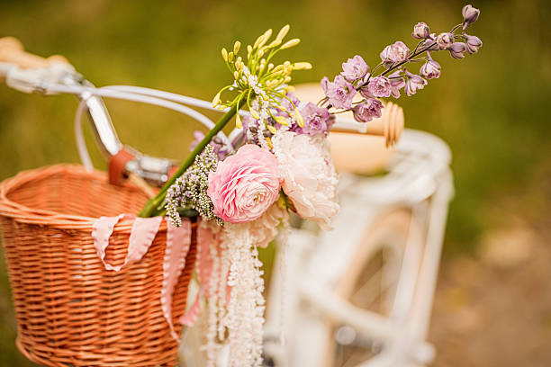 A vintage bicycle with a woven basket is decorated with vibrant flowers, including peonies and lilacs, sitting in a lush green park on a sunny day in spring.