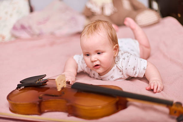 istock Curious baby girl examines violin on soft pink bedspread 2235895961