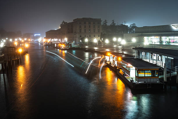 Long exposure captures the Grand Canal in Venice at night. Vaporetti create glowing trails amidst water reflections and city lights.
