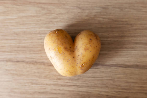 A heart-shaped potato sits on a wooden surface, displaying its unusual shape. This interesting vegetable can spark creativity in cooking or simply serves as a quirky decoration.