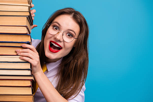 istock Cheerful young student expressing excitement while holding a stack of book against a blue background in a lively setting 2235898069