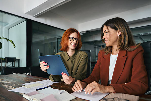 istock Two busy business women talking using tab working together at desk in office. 2235900858