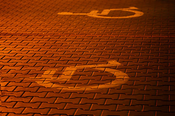 A glowing disability access symbol painted on a brick pavement, illuminated by streetlights at night. The scene emphasizes accessibility in public infrastructure and the importance of inclusive urban spaces for people with limited mobility.