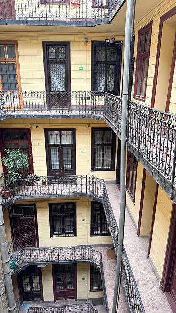 istock European courtyard view with multiple balconies, yellow facade, and potted greenery. Symmetrical old architecture with iron railings and retro residential character, typical urban housing design. 2235901206