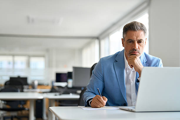 istock Busy serious middle aged business man working on laptop in office writing notes. 2235903646