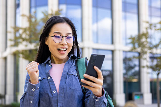 istock Excited Asian woman is smiling and holding her phone while looking at it. 2235906885
