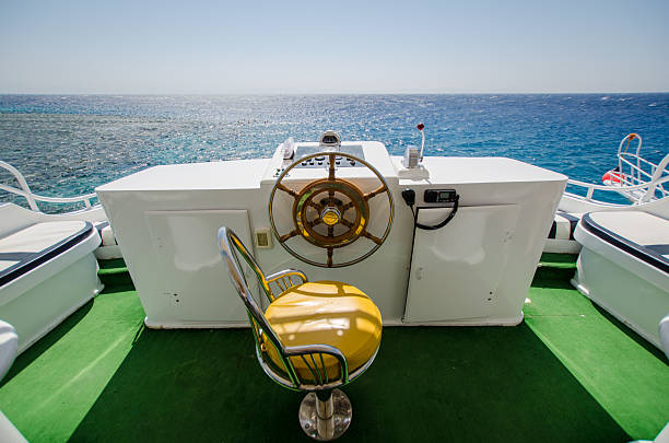 Luxurious yacht helm with vibrant green flooring and golden-brown seating. Overlooks expansive, sparkling Red Sea under clear blue sky. Sunlight reflects on waters surface