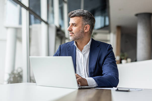 istock Businessman working on laptop and looking out window in modern office 2235913177