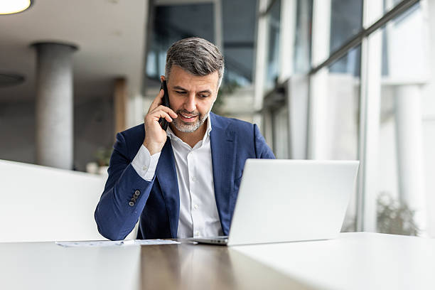 istock Businessman working on laptop and talking on phone in office 2235913197