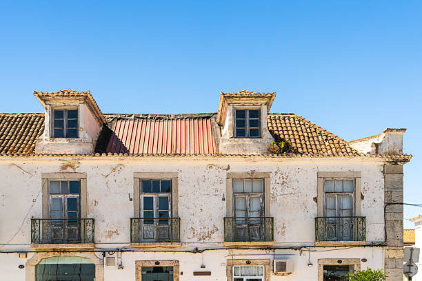 Old whitewashed building with peeling paint, tiled roof, and iron balconies under a clear blue sky.