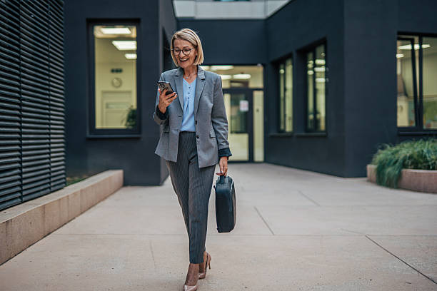 istock Smiling businesswoman walking and using smartphone outside office 2235920676
