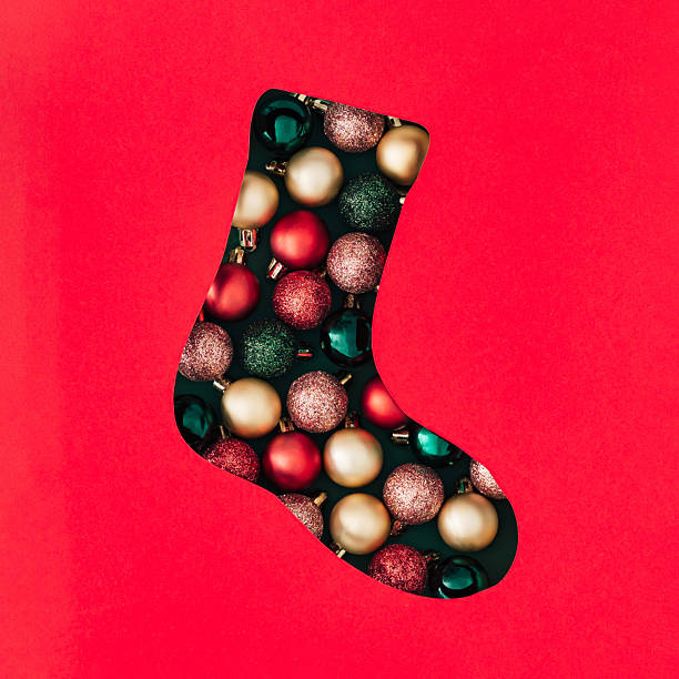 Winter composition with Xmas baubles visible through a Christmas stocking shaped gap on red background. Minimal Christmas and New Year concept. Creative festive holiday layout. Flat lay, top view.
