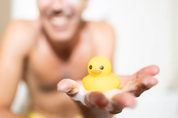 Cheerful man enjoys a relaxing foam bath, playfully holding a small yellow rubber duck in his soapy hand, adding a touch of childhood nostalgia to his self-care routine