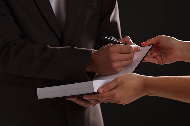 istock Writer signing autograph in book on black background, closeup 2235924985