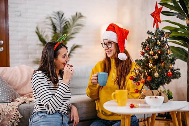 istock Two Female Friends Drinking Coffee And Eating Cookies While Talking On The Sofa During Christmas Holidays 2235928538